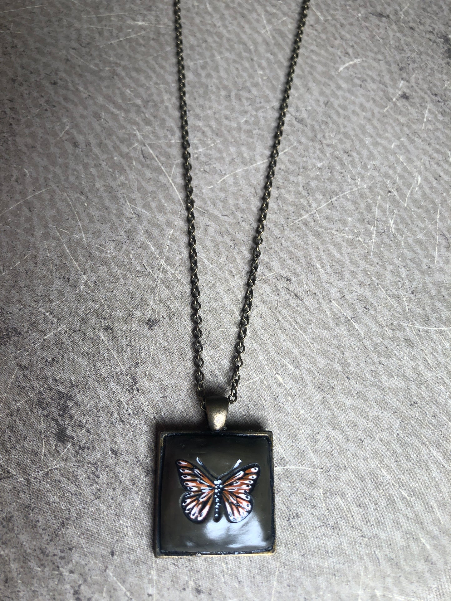 Hand Painted Monarch Style Butterfly on Deep Green Clay Nestled in 1” Square Antiqued Brass Setting Hung with 18” Coordinating Chain