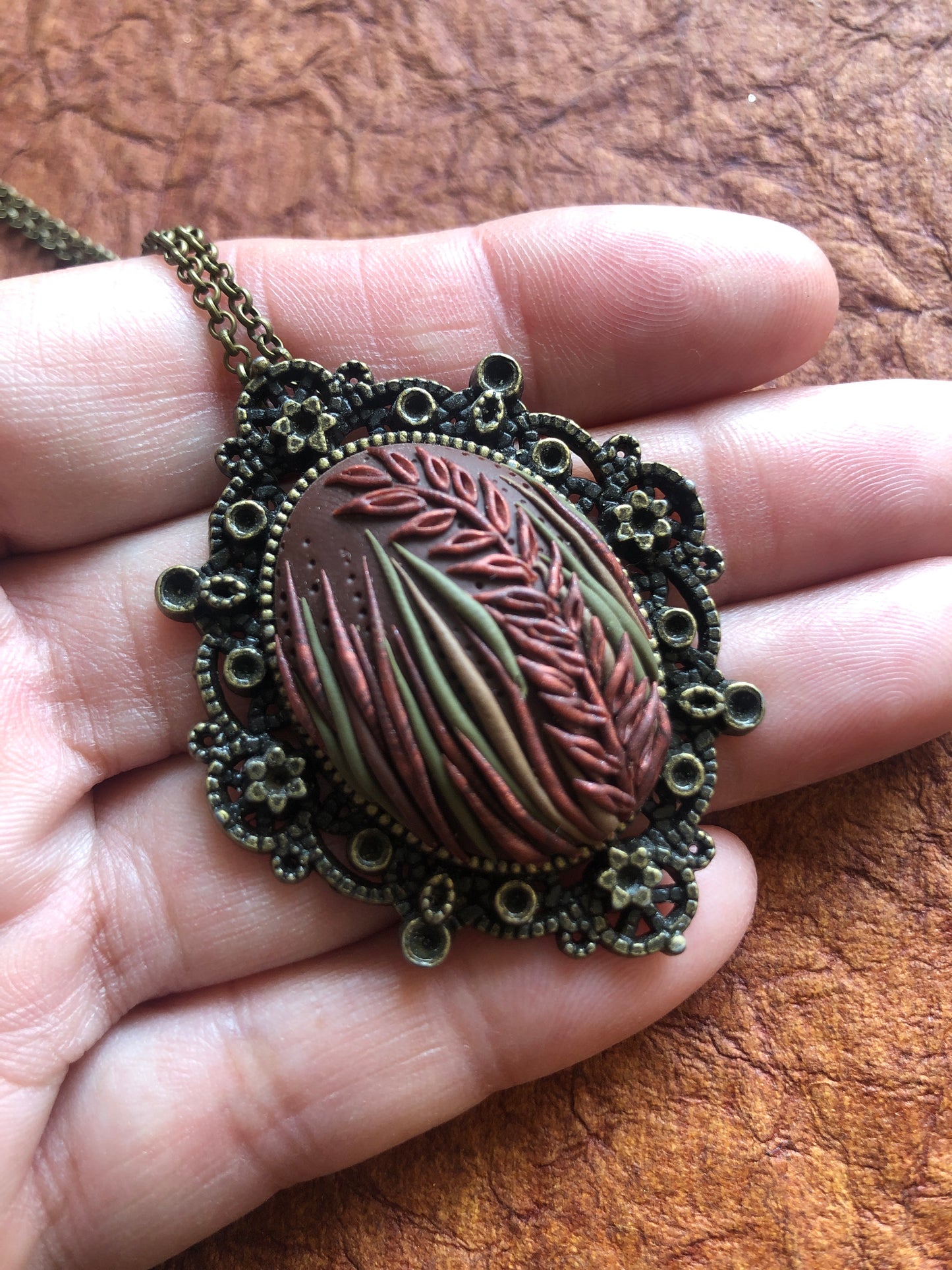 Hand carved tall grasses and leaves in brown, bronze and copper clay set in decorative pendant