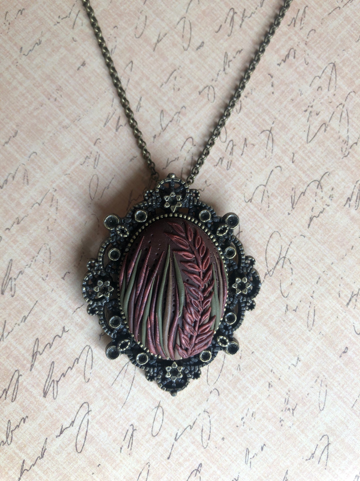 Hand carved tall grasses and leaves in brown, bronze and copper clay set in decorative pendant