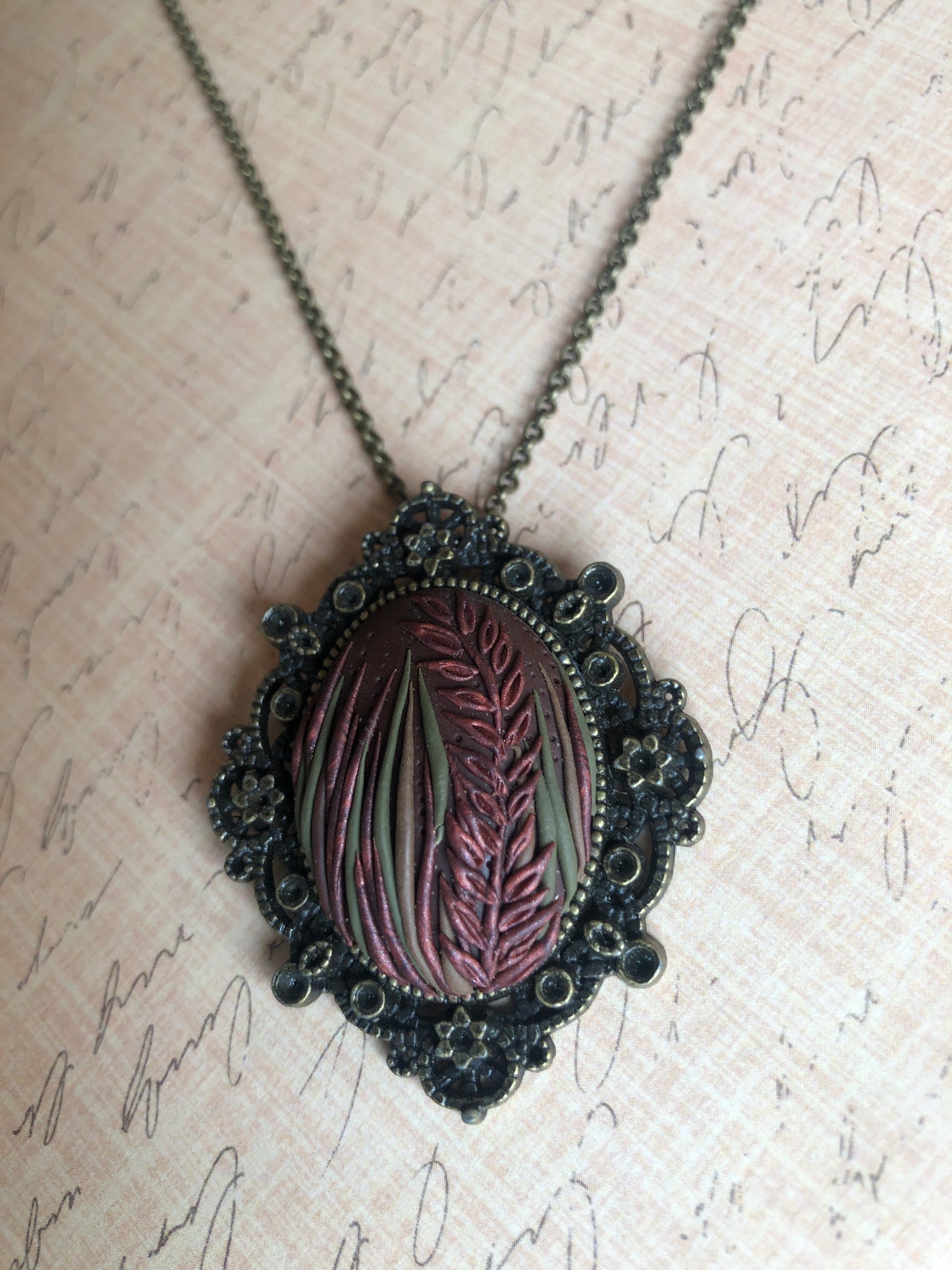 Hand carved tall grasses and leaves in brown, bronze and copper clay set in decorative pendant